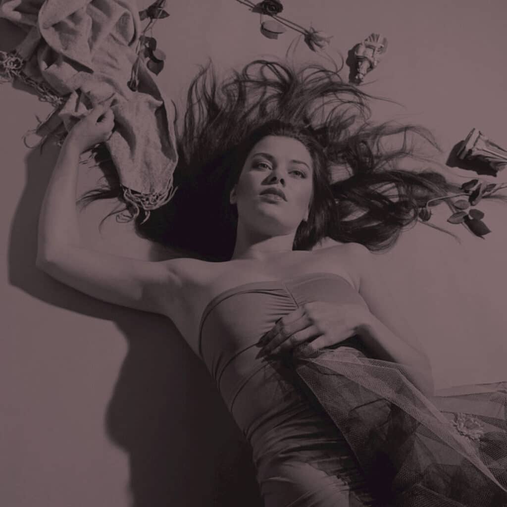 A young Candida Royalle lying down, her long dark hair spread around her, surrounded by flowers