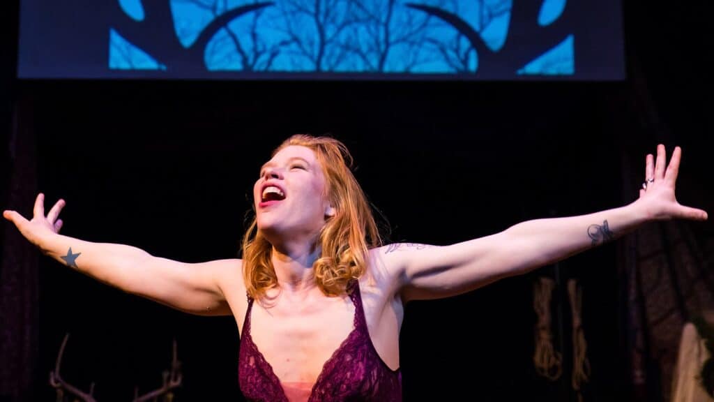 Madison Young on stage, arms wide open, in front of a screen showing deer antlers